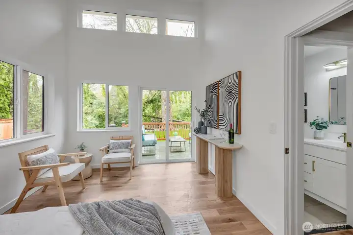 Breathtaking primary bedroom featuring soaring vaulted ceilings, walls of windows, and direct deck access overlooking a serene creek and wooded backyard and wide-plank hardwood laminate.