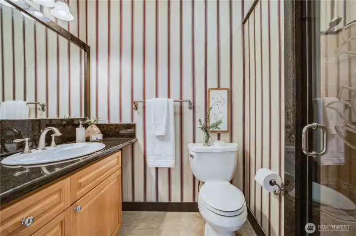 The main bathroom of the home is located in the hallway. It features stylish wallpaper, an upgraded vanity, a luxury shower with tile surround, and quality fixtures.