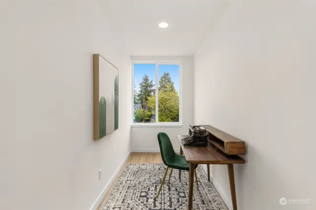 Work from home in this serene office space, featuring a large window with a view of the greenery outside, providing a calm and inspiring atmosphere.