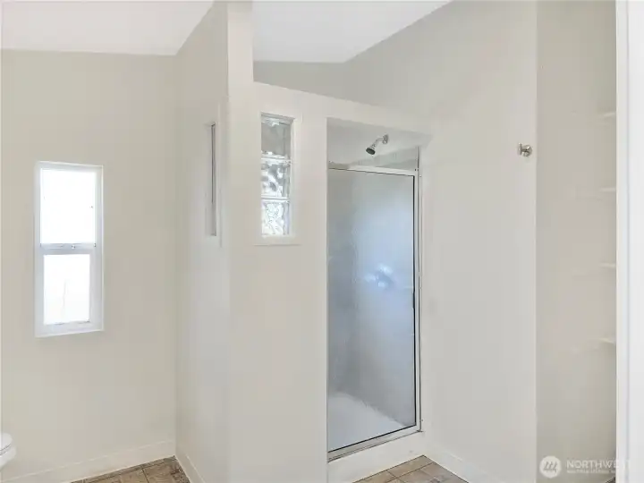 Spacious primary bath featuring a large tiled walk-in shower, linen storage, and natural light from glass block accents and a decorative window.