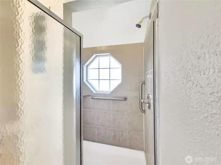 Primary bath featuring a large tiled walk-in shower with glass block accents that allow natural light while maintaining privacy, plus a decorative window for added character.