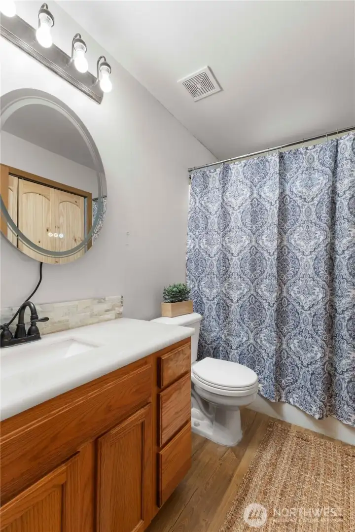 The main bath features laminate flooring, tile backsplash & a lighted hotel mirror