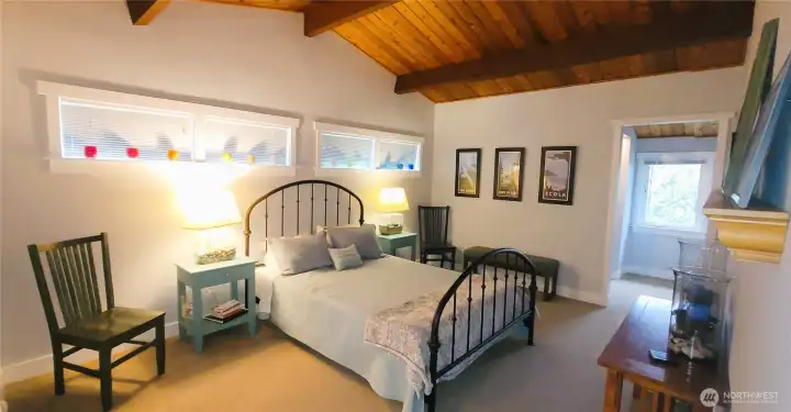 A spacious and serene primary suite featuring rich wood-beamed ceilings, an elegant ensuite with a deep jetted tub, a generous walk-in closet, dressing area, and a private sitting room—offering the perfect blend of comfort and coastal sophistication.