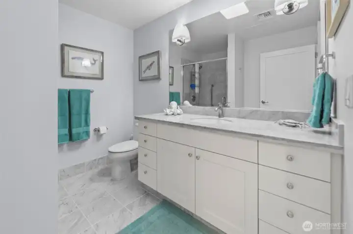 Primary 3/4 bathroom with walk in shower, marble floor and granite countertops.