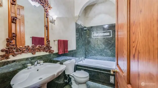 This luxurious bathroom on the main floor featuring intricate design details and high-end finishes. The rich green marble tiles create a sophisticated ambiance, beautifully complemented by the custom wood-framed mirror with ornate carvings.