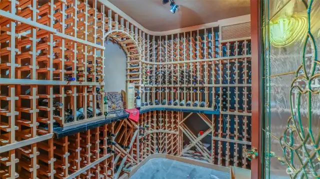 This custom, temperature-controlled wine cellar is a wine connoisseur's dream, offering ample storage for an extensive collection of bottles. Thoughtfully designed with elegant wood racks, the cellar provides both functionality and aesthetic appeal. The built-in shelving allows for easy organization and display of your finest vintages, while the climate-controlled environment ensures your wines are kept in optimal conditions. Whether you're an avid collector or simply enjoy entertaining, this wine cellar is the perfect addition to elevate your home. A stunning stained-glass door adds a touch of elegance and sophistication, creating a truly luxurious