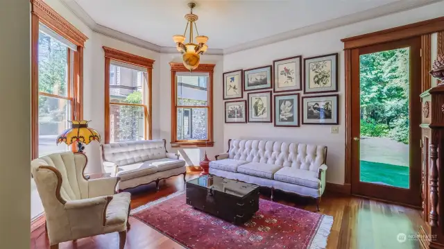 This charming living room features elegant wood detailing throughout, including ornate window casings and door frames that highlight the craftsmanship of the home.