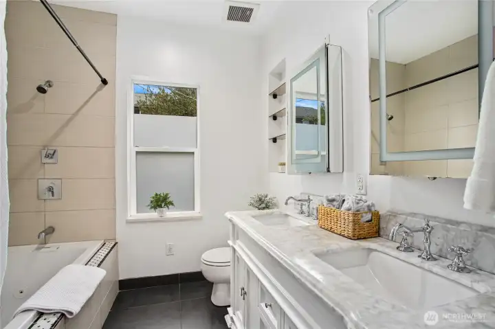 This spa-like bathroom offers a marble countertop vanity, double shower, spa tub, tile surround, and tiled floors.