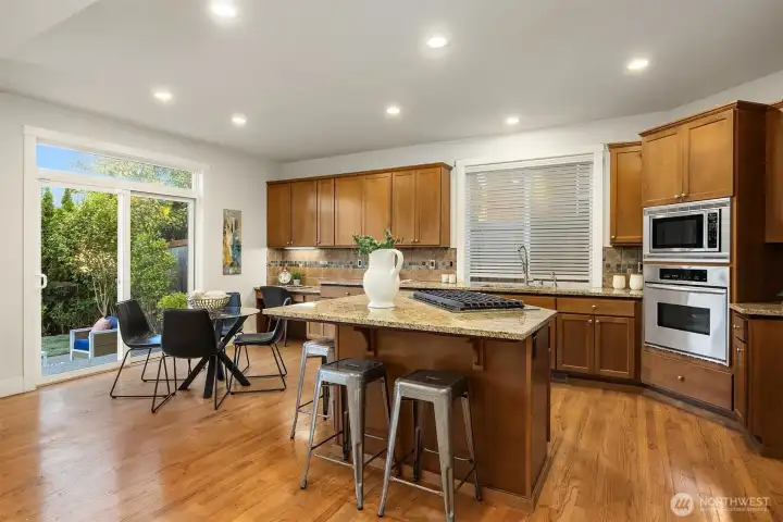 The spacious kitchen features granite slab countertops, stainless steel appliances, a 5-burner gas cooktop, a custom tile backsplash, walk-in pantry, and a large island with seating.