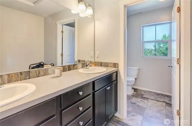 This full bathroom offers functionality and style with a dual-sink vanity, natural light, and a separate toilet area—perfect for busy mornings or sharing with ease.