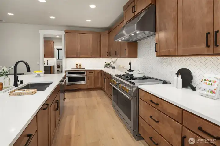 Canyon Creek maple cabinetry in a rich Toffee finish, soft-close drawers, pull-out shelving, quartz countertops, a herringbone backsplash, black-framed windows, and designer black fixtures create a timeless yet contemporary aesthetic.
