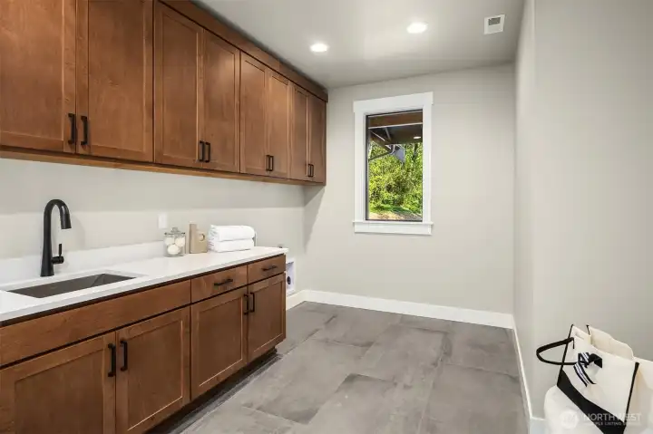 Spacious laundry room with built-in cabinetry, tile flooring, and a dedicated storage closet.