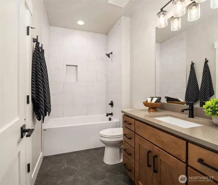 Well-appointed main-level bathroom featuring tile floors, a tile shower surround, and quartz countertops.