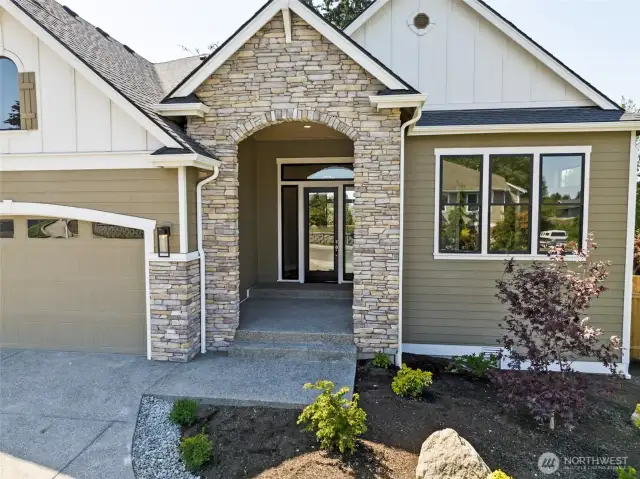 Through the decorative arched stone, an oversized covered front porch provides shelter for visitors and deliveries.