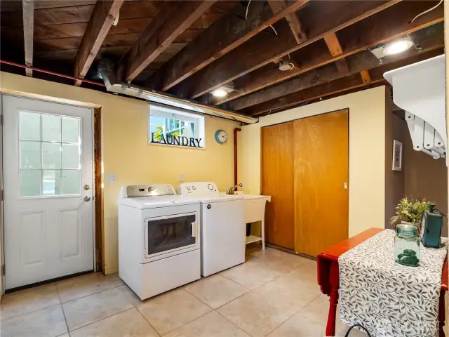 Lower level laundry room with tile flooring, utility sink and storage space; washer and dryer are included.