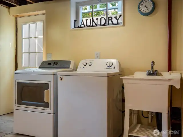 Lower level laundry room with tile flooring, utility sink and storage space; washer and dryer are included.
