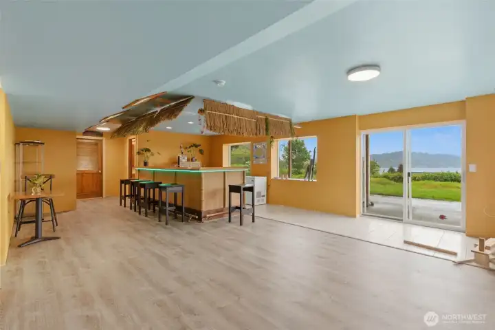 Lower-level tiki bar creates a fun, relaxed entertaining space with walkout access to the backyard for easy indoor/outdoor gatherings-the wood door leads to another office space.