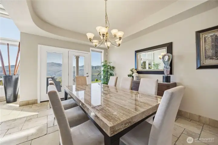 Elegant formal dining room with refined architectural details, including a tray ceiling and statement chandelier. Large windows and glass doors invite natural light while offering seamless access to outdoor living. Perfectly designed for hosting, this space blends sophistication and comfort for memorable gatherings.