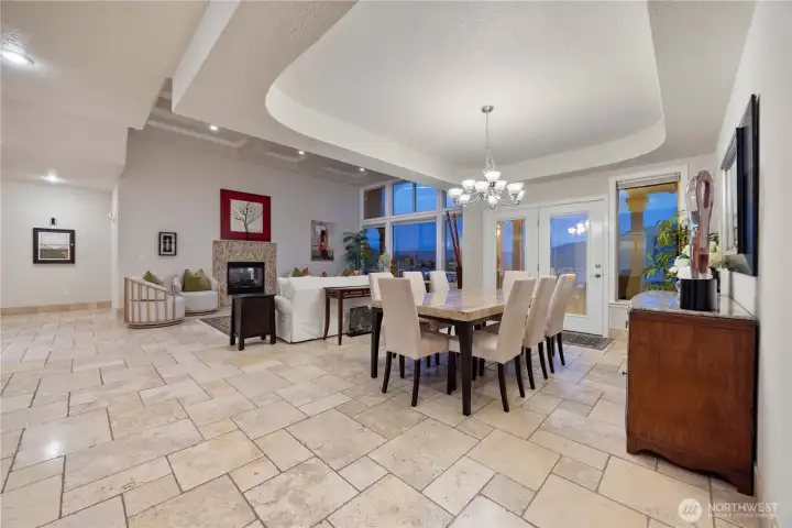 Spacious dining area featuring a beautifully detailed tray ceiling, elegant chandelier, and expansive tile flooring. This inviting space offers seamless flow to the living areas and is ideal for both everyday meals and larger gatherings, all enhanced by abundant natural light and a refined, open feel.