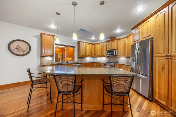 Well-appointed kitchen featuring rich wood cabinetry, granite countertops, and stainless steel appliances. The spacious peninsula with bar seating offers the perfect spot for casual dining or gathering, while the open layout flows seamlessly into the living areas—ideal for both everyday living and entertaining.