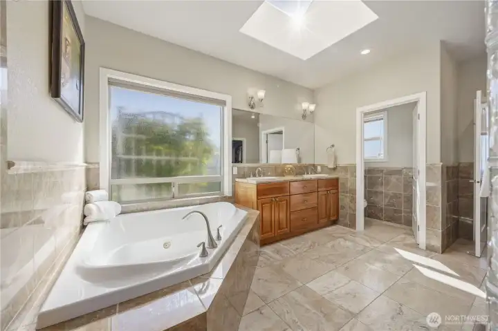Luxurious primary spa-inspired en suite featuring a soaking tub, expansive dual-sink vanity, and elegant tile flooring. Designed for relaxation, the space is filled with natural light and complemented by refined finishes, creating a serene and functional retreat.