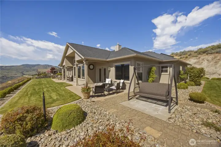 Beautifully designed exterior showcasing a spacious covered patio and meticulously landscaped grounds, all set against breathtaking panoramic views of Lake Chelan and the surrounding mountains. This inviting outdoor living space offers the perfect blend of privacy, comfort, and scenery for relaxing or entertaining year-round.