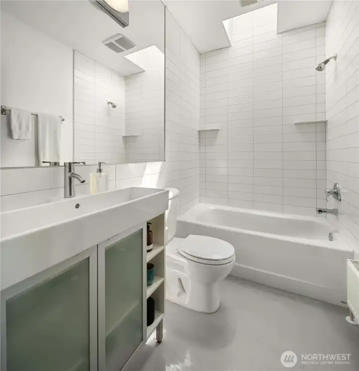 The secondary bath, serving the second bedroom, kitted out with a skylight and floor to ceiling tile.