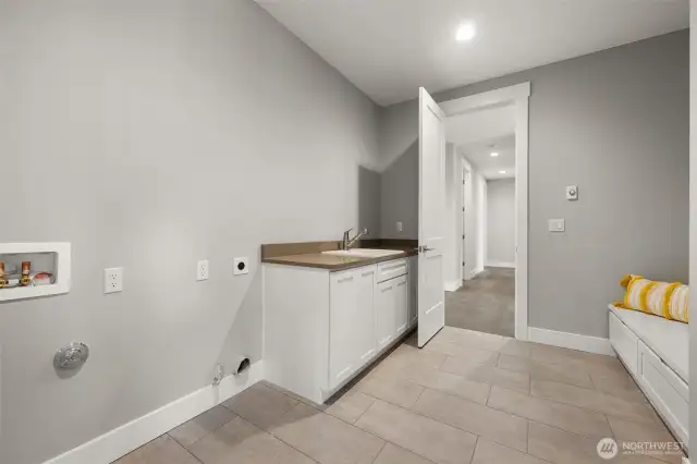 An oversized mud room provides not only plentiful laundry space, but also cabinetry, sink, & lovely built in storage bench.