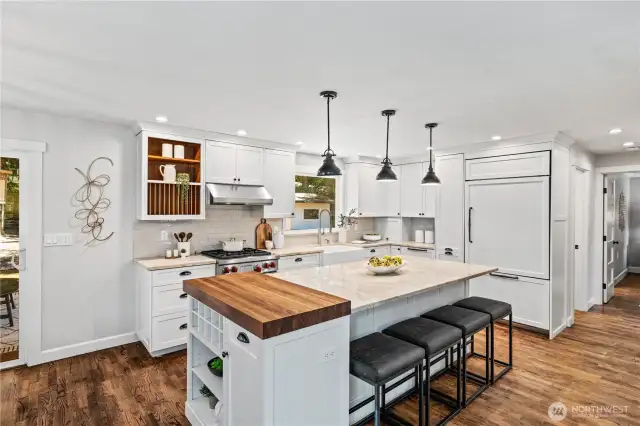 The custom kitchen is a chef’s dream, featuring a gas range, separate butcher block counter prep space, and a sleek refrigerator that integrates beautifully with the surrounding cabinetry