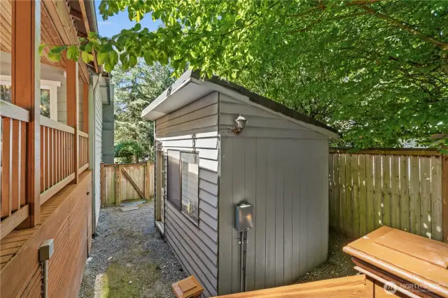 A shed/workshop sits on the side yard with built in shelving and counterspace for projects