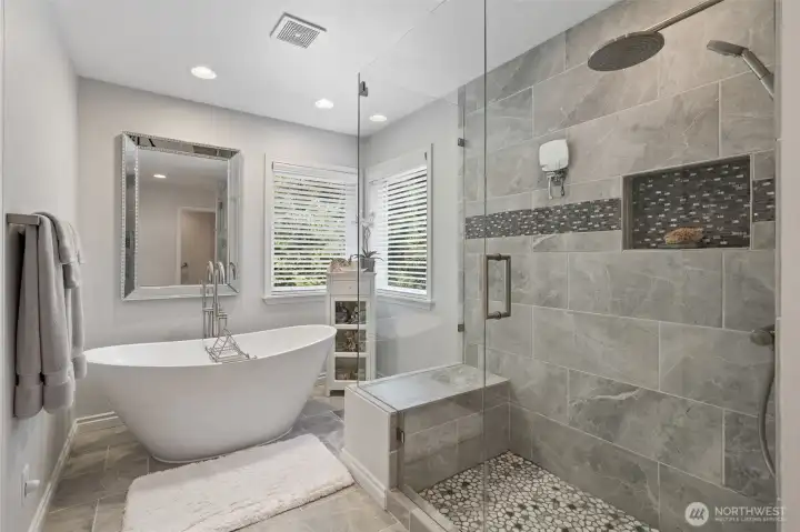 Natural light streams through windows, illuminating the elegant finishes, and the luxurious soaking tub. The large, glass-enclosed shower is highlighted, showcasing both style and functionality. This perspective emphasizes the serene, spa-like atmosphere that makes the primary suite a private retreat.