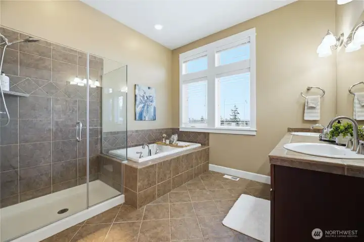 Relax in the spacious primary bath featuring a large soaking tub, separate walk-in tiled shower, dual sink vanity and abundant natural light