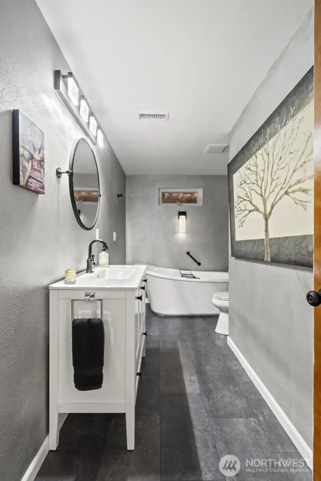 The lower level bathroom enjoys a freestanding soaking tub with handheld shower, a new vanity/sink, new plumbing and fixtures, and refreshed vinyl tile flooring.