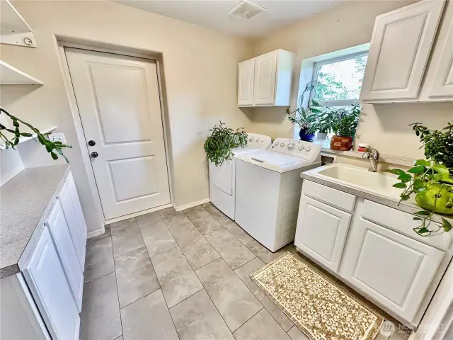 Located between the garage and kitchen sits the spacious laundry room complete with utility sink, cabinets and open shelves for extra storage space.