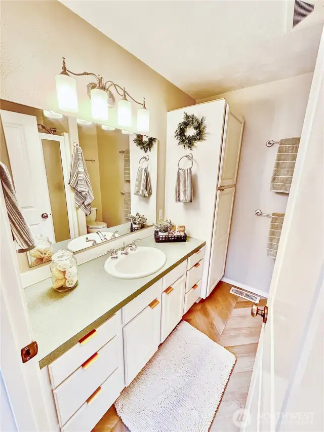 Attractive primary bath with linen cabinet and large shower with glass door.