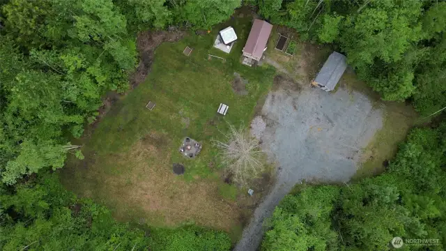 Aerial view showing the firepit area, horseshoes, cleared parking area, two sheds, raised garden beds and the hot tub.