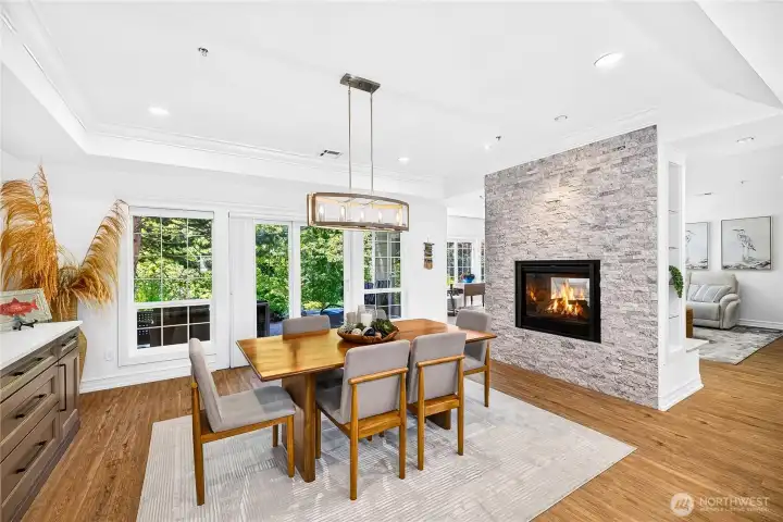 Open-concept living and dining area centered around a gas fireplace and surrounded by natural light.