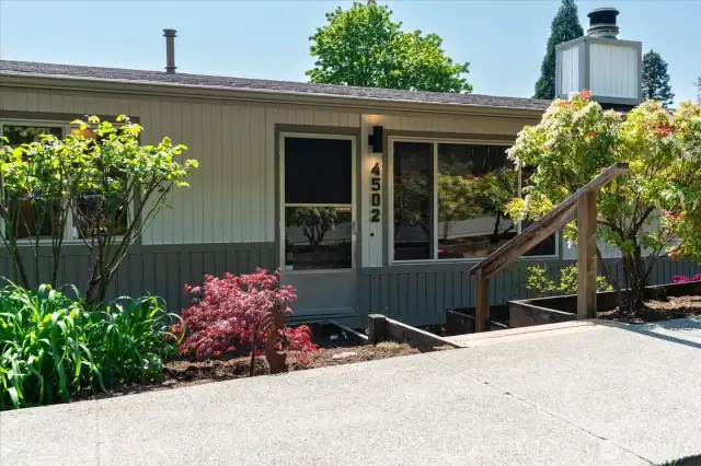 Mature landscaping lines the front steps and pathway guiding you inside