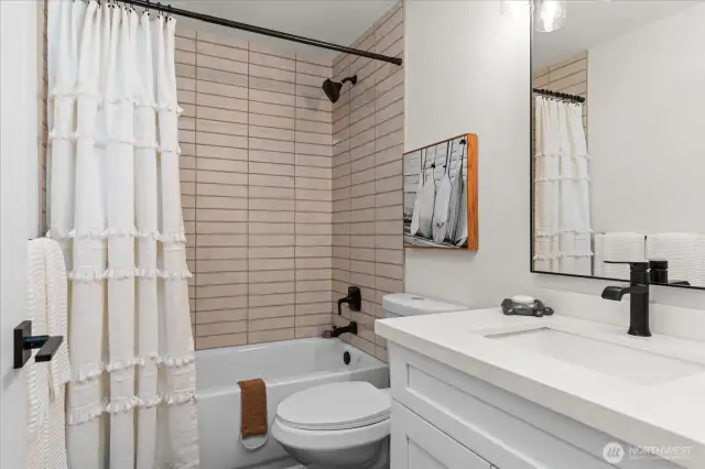 Tastefully appointed main full bath with white cabinets, quartz countertop, and subway tile tub surround