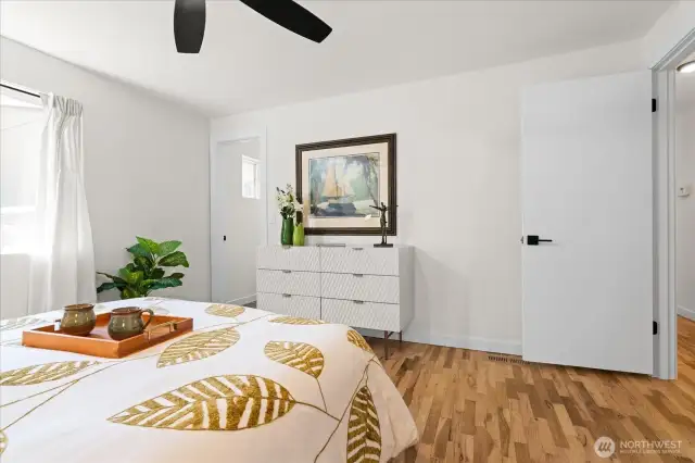 Primary suite with private half bath, hardwood flooring and ceiling fan feels inviting