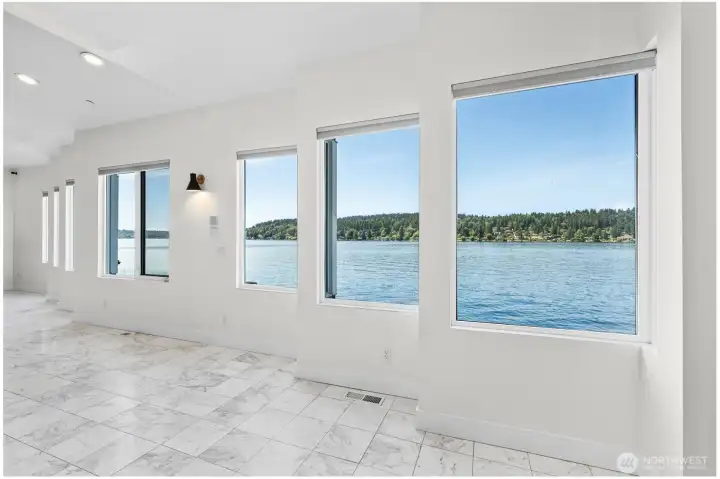 Expansive row of windows frame panoramic waterfront views, creating a dramatic backdrop throughout the second level living spaces. Marble flooring and a wall of windows bring the beauty of the water indoors, making every space feel connected to the shoreline.