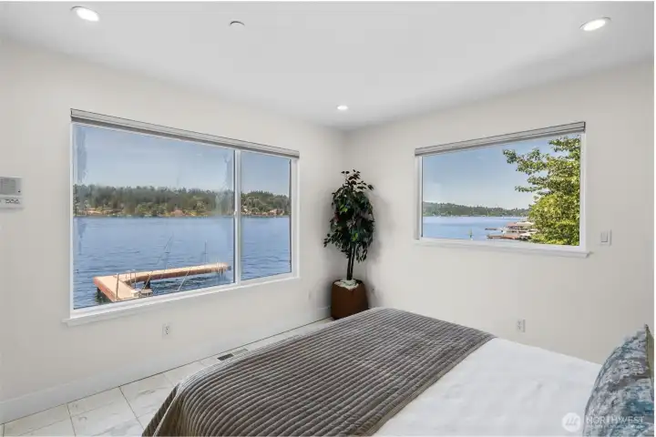 Main level bedroom captures beautiful waterfront views through oversized windows, creating a space where the scenery becomes part of everyday living. Wake up to views of the water and enjoy a connection to the waterfront from the comfort of your room.