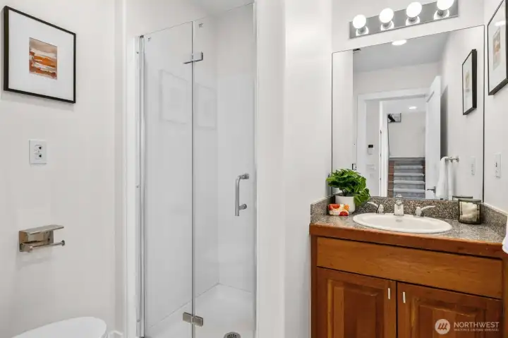 The main level bathroom features a walk-in shower with framless glass door, granite countertops, and warm wood cabinetry for a clean and timeless design. Positioned for convenience, this full bath offers comfort and functionality for guests and everyday living.