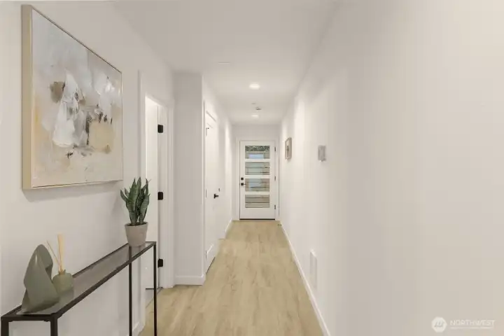 A bright, gallery-style hallway with light oak flooring and recessed lighting leads you into the home.