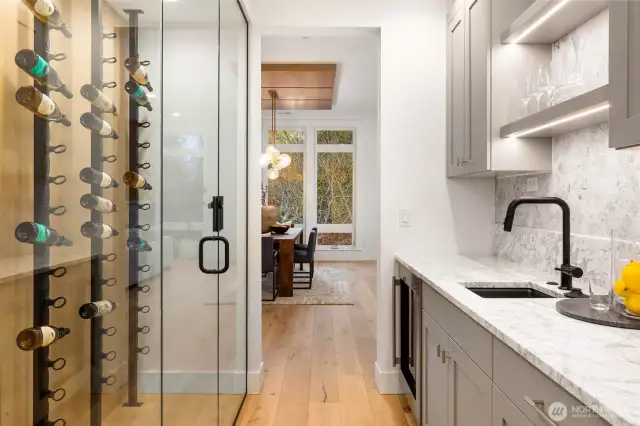 Stylish and sophisticated wet bar and wine room off dining. Wine room features custom metal racks, rift oak paneled walls, and frameless glass enclosure. Wet bar with custom lighting, desinger selected quartz counters and tile backsplash, prep sink, custom cabinets, and under counter beverage center
