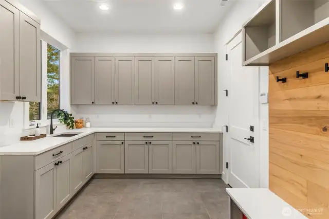 Large Utility room conveniently located just off oversize 3 car garage features desinger tile flooring, mudroom bench with hooks and she cubbies, custom cabinets with slab counters and tile backsplash, and stainless steel sink