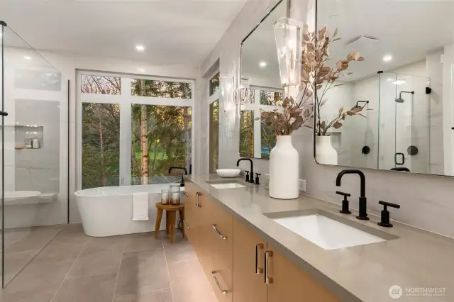 Luxurious Primary bath with floating vanities with toe lighting, floor to ceiling tile backsplash, freestanding soaking tub, and heated porcelain floors