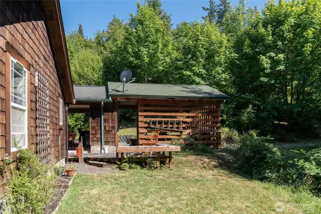 Back of home with small deck and built in seating. Woodshed and carport.