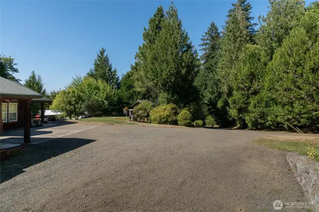 View from blueberries and corner of main level parking. Home and carport on left. Lower "tractor barn" shop can be seen beyond home.  Pumphouse in center of photo.