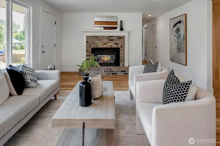 Bright and open living room featuring large picture windows, hardwood floors, and a fireplace centerpiece